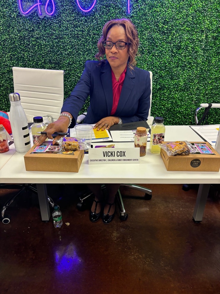 Vicki Cox seated at a panel with her Executive Director nameplate